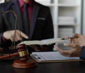 Two professionals in suits discussing legal documents with a judge's gavel and scales of justice on the table.