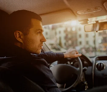 Man in dark clothing driving a car with sunlight streaming through the window.