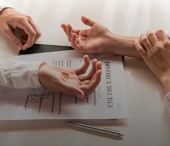 Two hands holding wedding rings over a divorce decree document on a table.