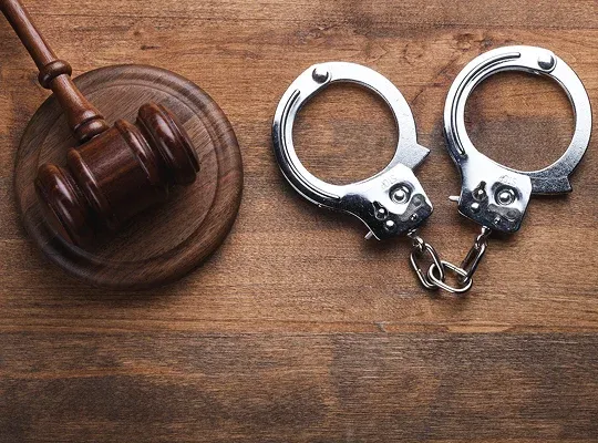 Wooden judge's gavel and silver handcuffs placed on a wooden surface.