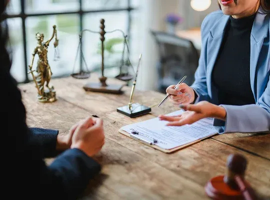 Two professionals discussing legal documents at a wooden desk with scales of justice.