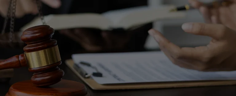 Wooden judge's gavel beside a clipboard with legal documents and a person's gesturing hand.