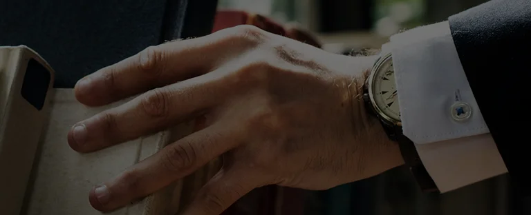 Close-up of a man's hand wearing a wristwatch, reaching for a book on a shelf.