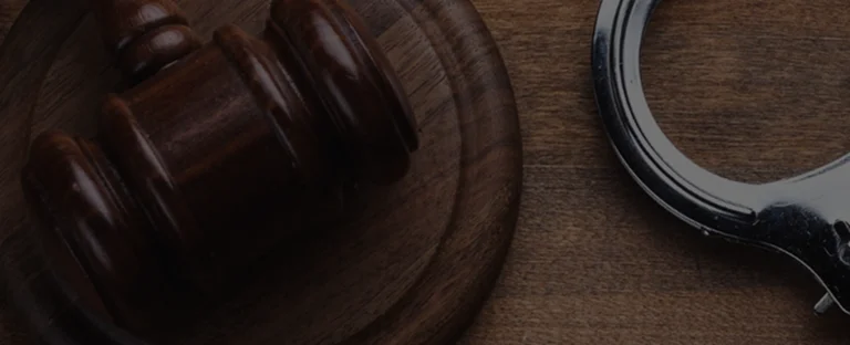 Close-up of a wooden judge's gavel and metal handcuffs on a dark wooden surface.
