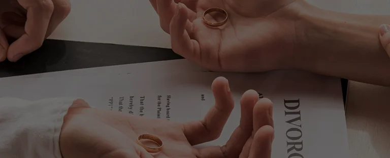 Hands holding wedding rings above a divorce document on a table.
