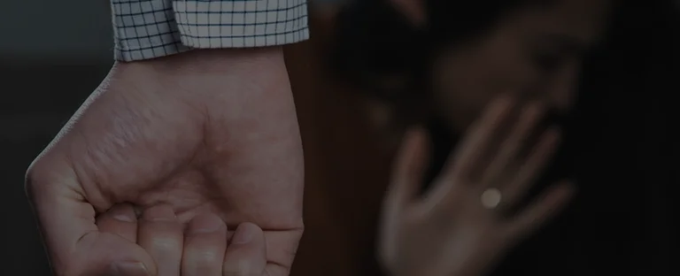 Close-up of a clenched fist with a blurred person in the background raising a hand defensively.