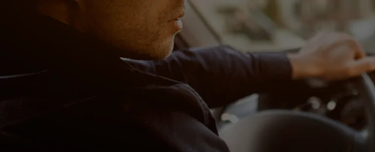 Close-up of a man in dark clothing driving a vehicle, focused on the road.
