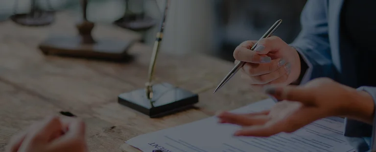 Close-up of two individuals discussing and signing a formal document on a wooden table.