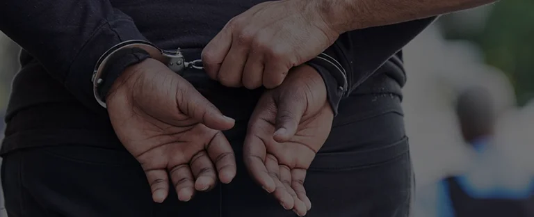 Close-up of a person’s hands cuffed behind their back with another person holding the handcuffs.