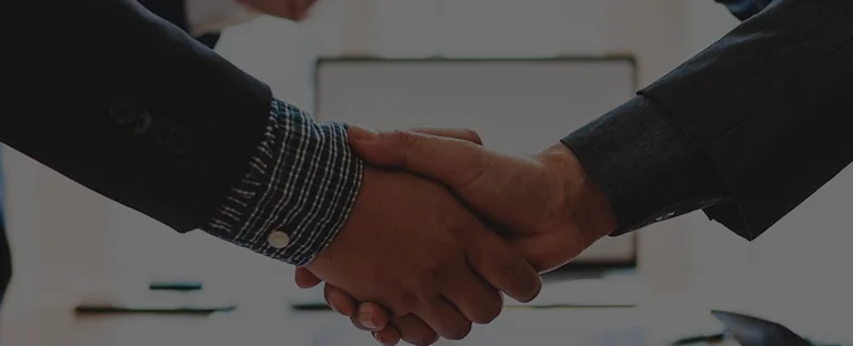 Two individuals wearing dark suits shaking hands in a professional setting.