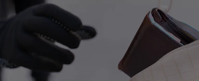 Close-up of a gloved hand reaching for a brown leather wallet inside a white textured bag.
