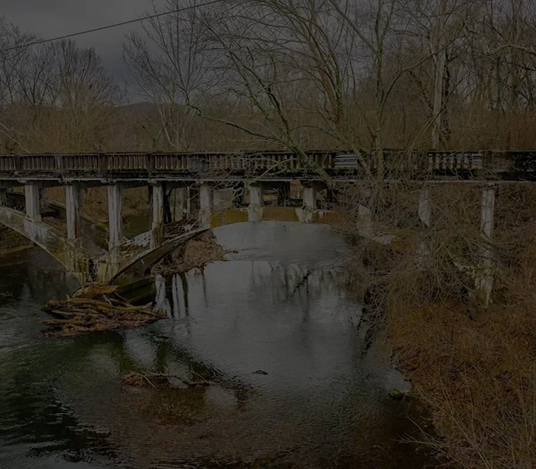 Concrete arch bridge over calm river surrounded by leafless trees in winter.