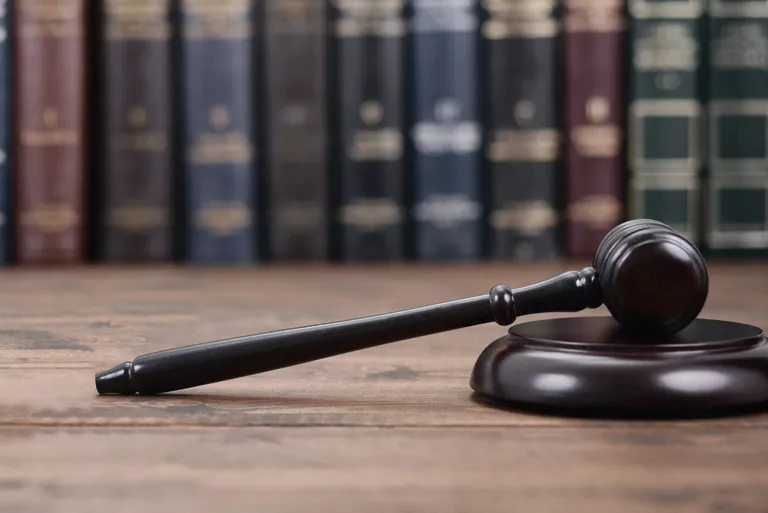 Wooden judge's gavel resting on sound block with blurred legal books in background.