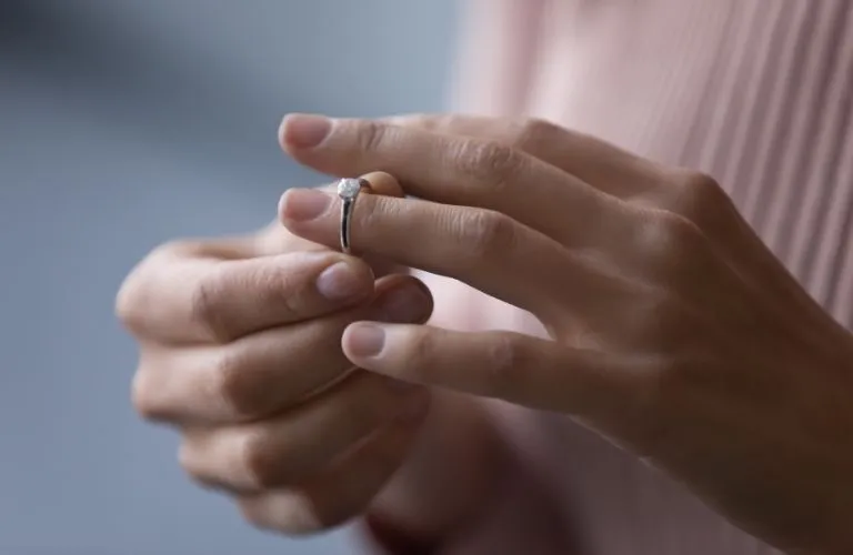 Close-up of hands removing a silver engagement ring with a clear gemstone on a finger.