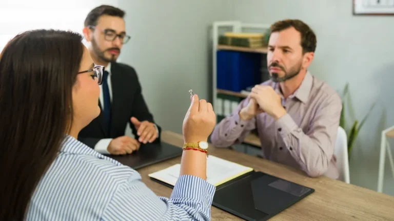 Three professionals in an office discussing an engagement ring during a meeting.