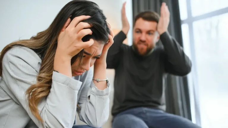 Frustrated man raising hands while woman holds head in distress indoors.