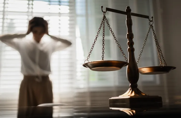Bronze balance scale in sharp focus with blurred woman adjusting hair in background.